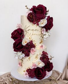 a three tiered wedding cake with red flowers on the top and white frosting