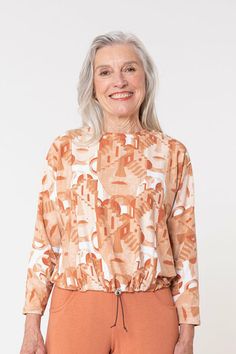 an older woman with grey hair wearing orange pants and a top that has abstract designs on it