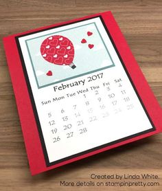 a calendar with a hot air balloon in the sky and hearts on it, sitting on a wooden surface