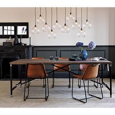 a dining room table and chairs with lights hanging from the ceiling above it, in front of a fireplace