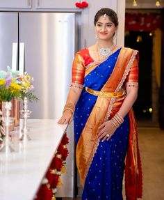 a woman in a blue and orange sari standing next to a counter with flowers on it