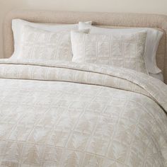 a white bed with two pillows on top of it next to a beige headboard