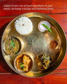 a metal plate topped with different types of food on top of a wooden table next to rice