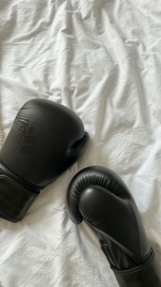 two black boxing gloves laying on top of a white sheet