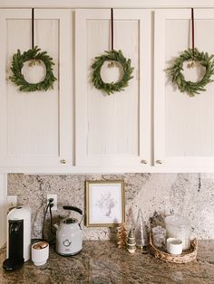 two wreaths hanging on the wall above a kitchen counter with coffee maker and other items