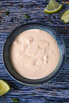 a bowl filled with white sauce next to sliced limes on a blue tablecloth