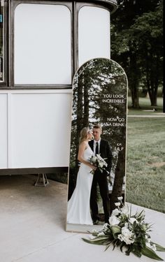 a bride and groom standing in front of a mirror with their wedding photos on it