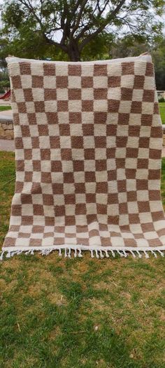 a brown and white checkered blanket sitting on top of a grass covered field next to a tree