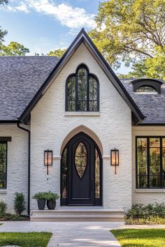 a white brick house with black trim and arched windows, two potted plants on the front porch