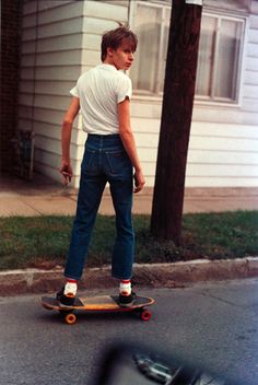 a young boy riding a skateboard down the street in front of a house and car