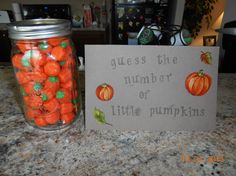 a jar filled with orange candies next to a sign that says guess the number of little pumpkins