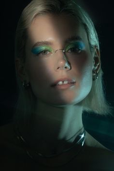 a woman with green and blue makeup is posing for a photo in front of a dark background