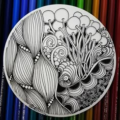 a drawing on a plate with colored pencils in the back ground and an image of flowers