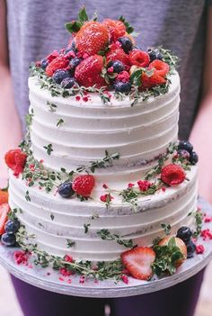 a white cake topped with berries and greenery on top of a purple platter