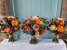 three bouquets of colorful flowers are sitting on a white tablecloth in front of a blue door