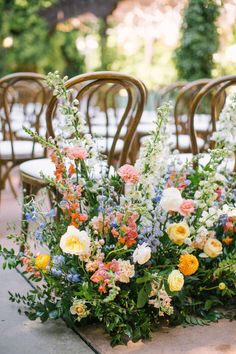 an arrangement of flowers and greenery on the ground in front of chairs at a wedding