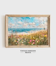 a painting hanging on the wall with flowers in front of it and an ocean view