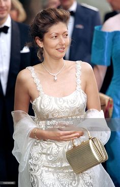 a woman wearing a white dress and holding a gold purse in her hand while walking down the