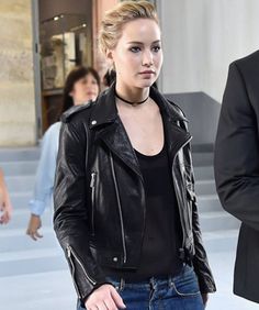 a woman in black jacket and jeans walking down the street