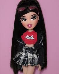 a doll with long black hair wearing a red shirt and plaid skirt, standing in front of a pink background