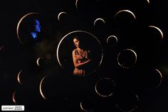 a woman standing in front of a black background with circles around her and a man looking at the camera