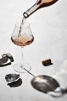 a person pouring wine into a glass on top of a table with spoons and corks