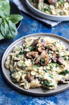 pasta with mushrooms, spinach and cheese on a blue tablecloth next to another dish