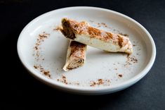 two pieces of food on a white plate covered in powdered sugar and brown flakes