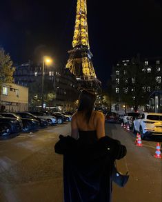 a woman standing in front of the eiffel tower at night with her back to the camera