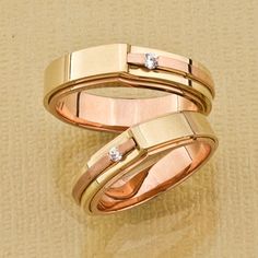 two gold wedding bands with diamonds on them sitting on a beige surface in front of a tan background