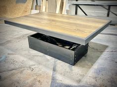 a coffee table with an open drawer in the middle on concrete flooring next to wooden planks