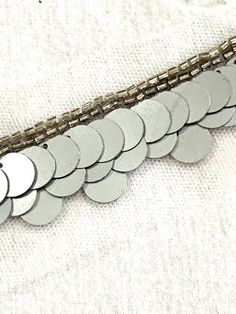 a close up of a metal chain on a white cloth with lots of silver circles