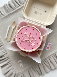 a pink birthday cake sitting on top of a table next to a fork and knife