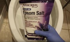 a person holding up a tube of epsom salt in front of a toilet bowl