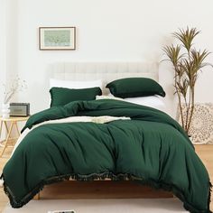 a bed with green comforter and pillows in a white room next to a potted plant