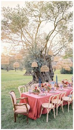 an outdoor table set up with pink linens and blue candlesticks in front of a large tree