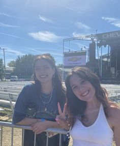 two girls standing next to each other in front of a metal fence at a concert