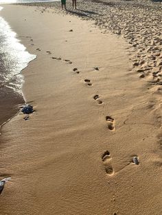 two people walking along the beach with footprints in the sand