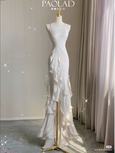 a white dress on a mannequin stand in front of curtained windows with the words paolad written above it