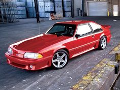 a red sports car parked in front of a loading dock at an industrial facility or warehouse