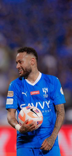 a man holding a soccer ball in his hand and smiling at the camera while wearing a blue uniform