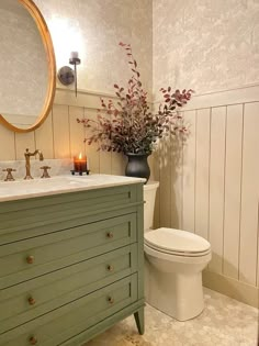 a white toilet sitting next to a green dresser in a bathroom under a round mirror