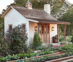 a small white house surrounded by greenery and flowers