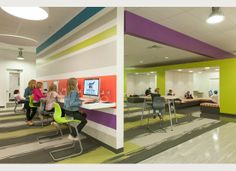 people sitting at desks in an office with computers on the wall and colorful walls