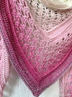 a pink and white crocheted shawl hanging on a wall