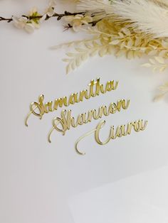 two name cut out on top of a white surface next to some flowers and feathers