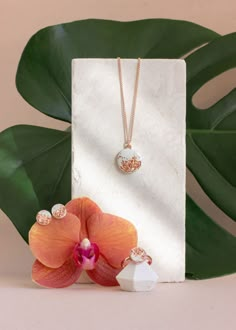 two necklaces on display next to a flower