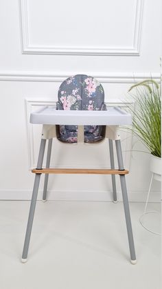 a high chair with a flowered seat cover on it and a potted plant in the background