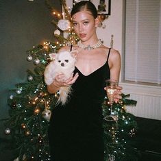 a woman holding a small dog in front of a christmas tree