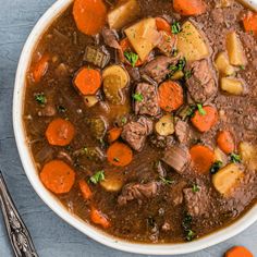 a bowl of beef stew with carrots, potatoes and parsley on the side